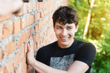 Mutlu bir genç, eski bir tuğla evin yanında dinlenir ve samimi bir şekilde gülümser ve başka tarafa bakar, bir gencin hayatının mutlu anları, çocuğun güzel beyaz dişleri ve koyu renk saçları vardır.