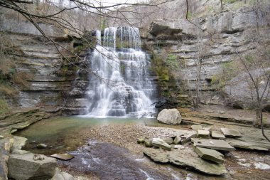 Görüntü, etrafındaki kayaları kaplayan ince bir örtüyle akan suyun dinamizmini yakalar. Şimdi yapraklarının çoğunu koparmış olan ağaçlar doğal olarak manzarayı çerçevelediler ve karmaşık dallardan mavi gökyüzünü ortaya çıkardılar.