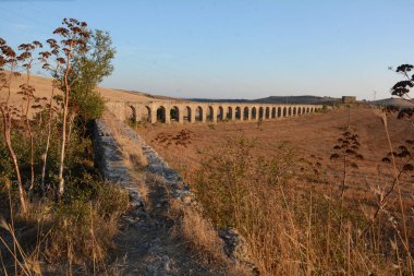 Nefes kesen bir günbatımı, Monte Romano 'daki antik Roma su kemeri kalıntılarının üzerine sıcak, altın rengi döküyor. Yıpranmış taş kemerler dimdik, renkli gökyüzüne karşı siluet, tarih ve ebedi güzelliği çağrıştırıyor..