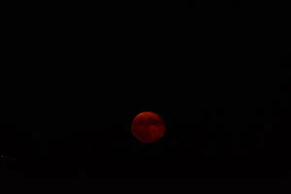 stock image A mesmerizing red moon glows brightly in the dark night sky, casting an eerie yet beautiful light over the landscape. The celestial body appears otherworldly, with its crimson hue creating a stunning contrast against the black sky and distant stars.