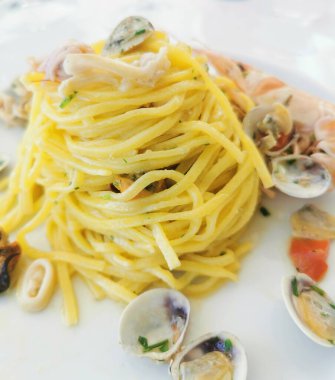  Beyaz bir tabakta servis edilen midye, karides ve muhtemelen mürekkep balığı da dahil olmak üzere karışık deniz ürünleri içeren lezzetli bir spagetti tabağı.