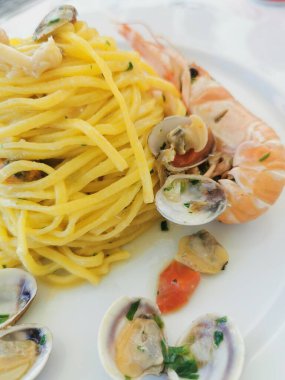  Beyaz bir tabakta servis edilen midye, karides ve muhtemelen mürekkep balığı da dahil olmak üzere karışık deniz ürünleri içeren lezzetli bir spagetti tabağı.