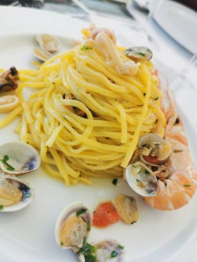  Beyaz bir tabakta servis edilen midye, karides ve muhtemelen mürekkep balığı da dahil olmak üzere karışık deniz ürünleri içeren lezzetli bir spagetti tabağı.