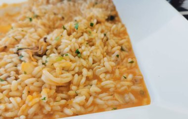 Lezzetli bir son için taze maydanozla süslenmiş midye, kalamar ve zengin deniz ürünleri çorbasıyla mükemmel pişirilmiş yumuşak pirinçli kremalı deniz ürünleri pilavı.