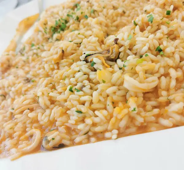 Lezzetli bir son için taze maydanozla süslenmiş midye, kalamar ve zengin deniz ürünleri çorbasıyla mükemmel pişirilmiş yumuşak pirinçli kremalı deniz ürünleri pilavı.