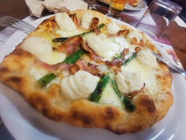 İçinde kremalı ricotta kıvrımları, çıtır domuz pastırması, taze kuşkonmaz ve kahverengi kabuklu erimiş peynir olan lezzetli bir zanaatkar pizza. Mükemmel pişmiş ve lezzetten patlıyor..