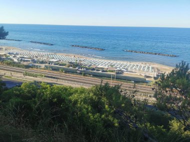Yukarıdan çekilen bu canlı yaz manzarası Fano 'daki Fosse Sejore plajına bakıyor. Kıyı şeridi, altın kum boyunca düzgünce dizilmiş renkli şemsiyeler ve güneşliklerle dolu. Adriyatik 'in sakin, berrak suları...