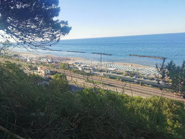 Yukarıdan çekilen bu canlı yaz manzarası Fano 'daki Fosse Sejore plajına bakıyor. Kıyı şeridi, altın kum boyunca düzgünce dizilmiş renkli şemsiyeler ve güneşliklerle dolu. Adriyatik 'in sakin, berrak suları...