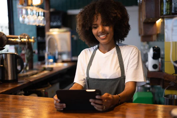 在检查平板电脑上的订单时 头发为非洲裔的年轻女服务员笑着 — 图库照片