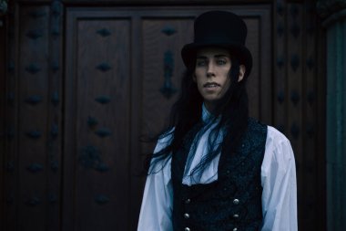 Uzun siyah saçlı, gotik kostümlü, antik ahşap kapılı yakışıklı vampirin portresi.