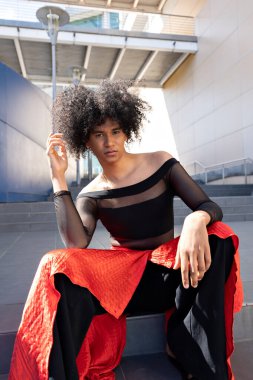 Siyah ve kırmızı elbiseli Latin kökenli çift cinsiyetli afro saçlı..