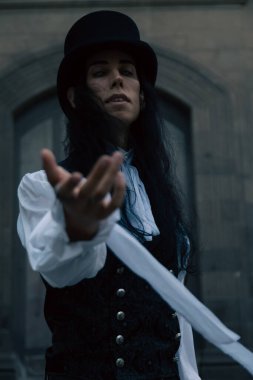 Uzun siyah saçlı, silindir şapka takan gizemli gotik vampir elini uzatıyor.