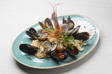 Dev karides ve doğranmış maydanozla kaplı kremalı risotto. Canlı turkuaz seramik tabakta dinleniyor.