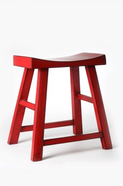 Tahtadan yapılmış eğimli bir tabure ve kırmızıya boyanmış basit ama zarif bir mobilya parçası yaratıyor.