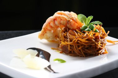 Deniz mahsulleri fideua lezzetli karidesler, yeşil bezelyeler, taze nane, saf seramik yüzeyde sanatsal sosla kaplanmış.