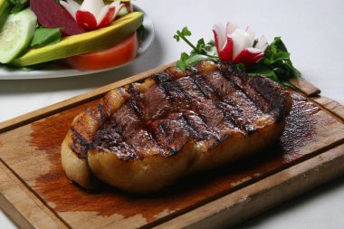 Meyveli ızgara picanha bifteği ahşap kesim tahtasının üzerinde duruyor, yanında da taze salata.