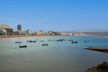 Las Canteras Sahili 'nin kumlu kıyı şeridi boyunca demirlemiş renkli balıkçı gemileri, Büyük Kanarya, sahil manzarasının arkasına kurulmuş kentsel ufuk çizgisi