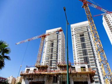 İsrail 'de inşaat halindeki çok katlı beton bina, mavi gökyüzüne karşı vinçler.
