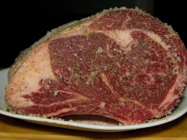 Beef prime rib roast in stages of preparation: seasoning