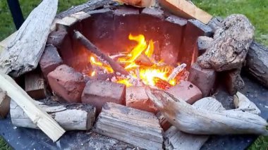 Tuğlalar ve alevleri çevreleyen yakacak odunlarla dolu bir ateş deposunda şenlik ateşi. Kadının eli ateşe bir parça odun ekler.