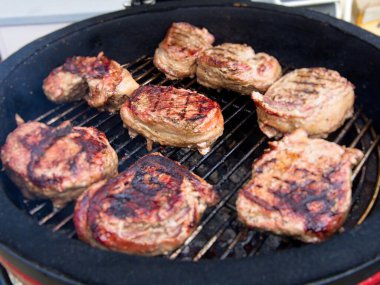 Tournedo biftekleri kömür ızgarasında pişiyor. Orta pişmiş, kömürleşmiş ızgara izleri görülüyor.