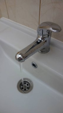 Close-up of a chrome faucet with running water in a white ceramic sink. clipart