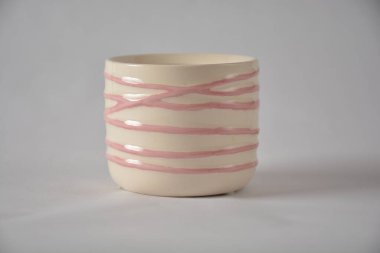 Beyaz arka planda pembe desenli çizgileri olan el yapımı seramik bardak..