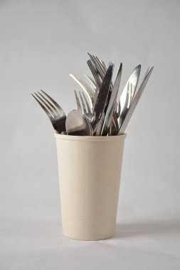 Eğik beyaz bir bardaktan sade bir zemine dökülen çatal ve bıçakların sanatsal görüntüsü.