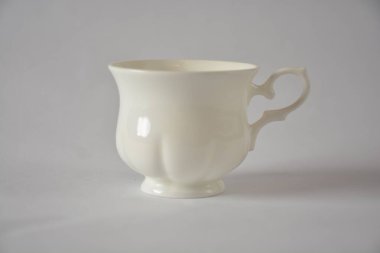 Elegant ivory porcelain teacup with a delicate curved handle on a soft gray background. clipart