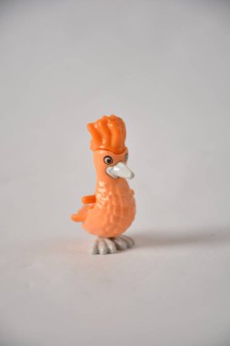 Orange plastic bird toy on a white wall, appearing playfully stuck headfirst. clipart