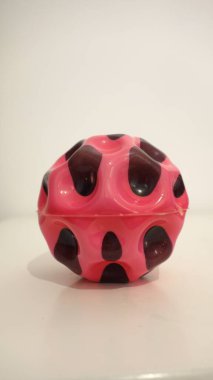 Colorful plastic toy ball with pink and black pattern on a white surface. clipart