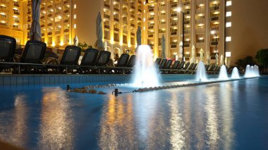 Geceleri çeşmeleri olan zarif bir otel havuzu.