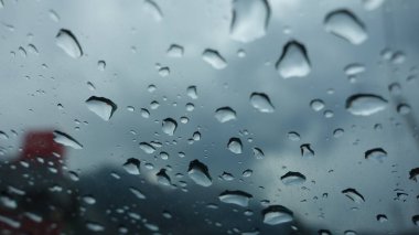 Bulutlu arkaplanı olan bir pencereye yağmur damlaları.