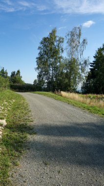 Açık mavi gökyüzünün altında manzaralı kırsal yol.