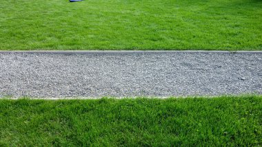 Çimenlerin arasından geçen çakıl yolu.