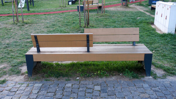 Современная двухсторонняя деревянная скамейка в парке на траве.