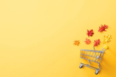 Sarı masa arkasında akçaağaç yaprakları ve alışveriş arabası olan sonbahar alışveriş tasarımı kavramı.