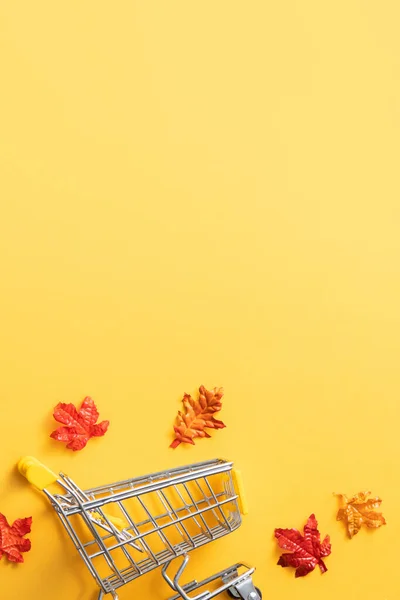 黄色のテーブルの上にショッピングカートとカエデの葉を持つ秋のショッピングデザインコンセプト — ストック写真
