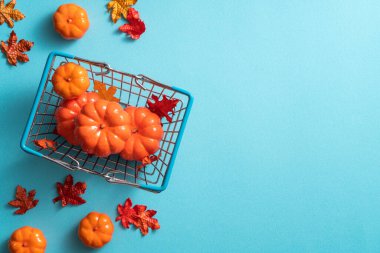 Alışveriş arabası, akçaağaç yaprakları ve mavi masa arkasında balkabağı olan sonbahar alışveriş tasarımı konsepti.