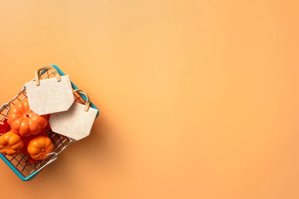 stock image Autumn shopping design concept with shopping cart, maple leaves and pumpkin on orange table background.