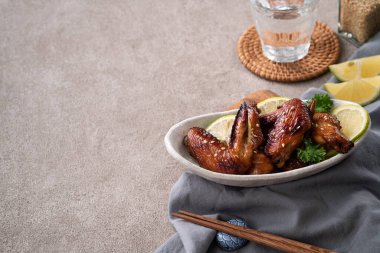Kızarmış tatlı soslu teriyaki tavuk kanatlarını gri masa arkasında beyaz bir tabakta kapat..