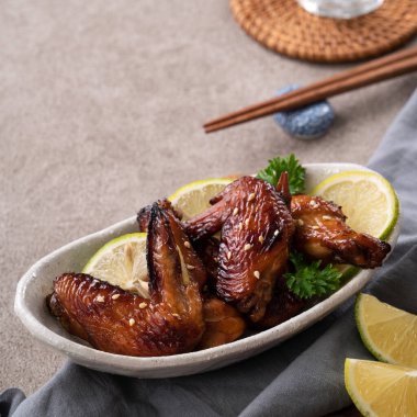 Kızarmış tatlı soslu teriyaki tavuk kanatlarını gri masa arkasında beyaz bir tabakta kapat..