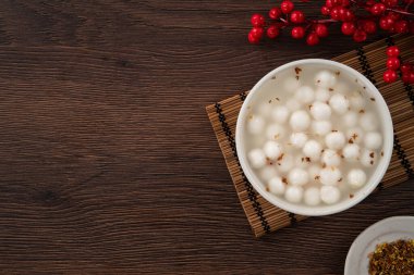 Küçük beyaz tangyuan (tang yuan, glutinous rice dumpling balls) tatlı osmanthus balı ve ahşap masa arkasındaki bir kasede şurup çorbası.