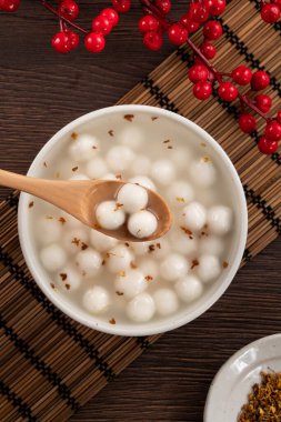 Küçük beyaz tangyuan (tang yuan, glutinous rice dumpling balls) tatlı osmanthus balı ve ahşap masa arkasındaki bir kasede şurup çorbası.