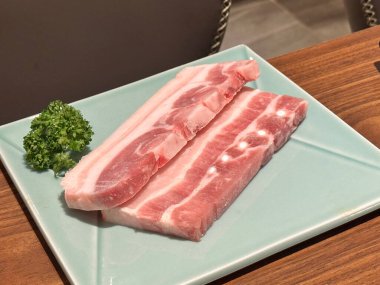 Grilling pork belly meat on a round iron BBQ net in restaurant for eating, fresh delicious food cuisine lifestyle.