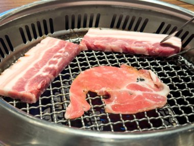 Grilling pork belly meat on a round iron BBQ net in restaurant for eating, fresh delicious food cuisine lifestyle.
