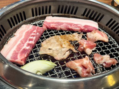Grilling pork belly meat on a round iron BBQ net in restaurant for eating, fresh delicious food cuisine lifestyle.