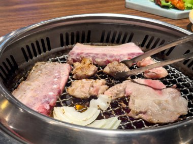 Grilling pork belly meat on a round iron BBQ net in restaurant for eating, fresh delicious food cuisine lifestyle.