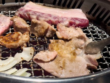 Grilling pork belly meat on a round iron BBQ net in restaurant for eating, fresh delicious food cuisine lifestyle.