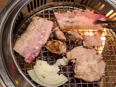 Grilling pork belly meat on a round iron BBQ net in restaurant for eating, fresh delicious food cuisine lifestyle.